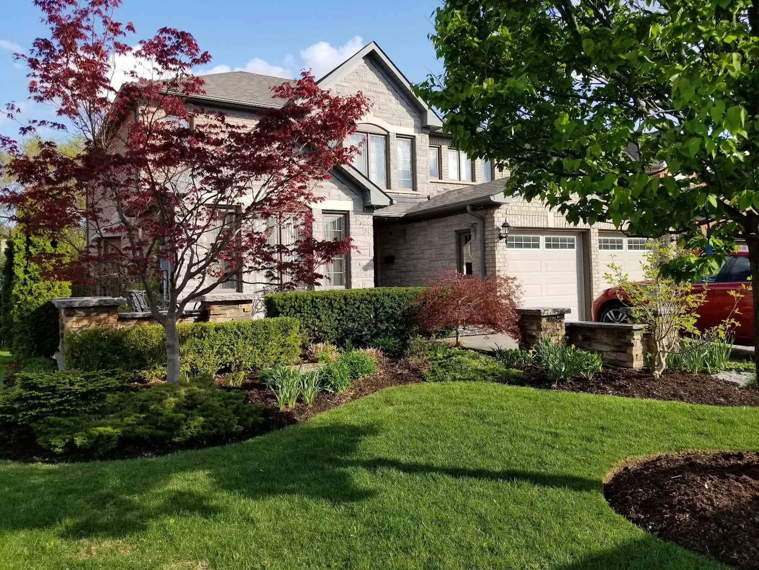 Front entrance landscaping in Hamilton, Ontario with stone pillars, Japanese maple, manicured lawn, and planted garden beds