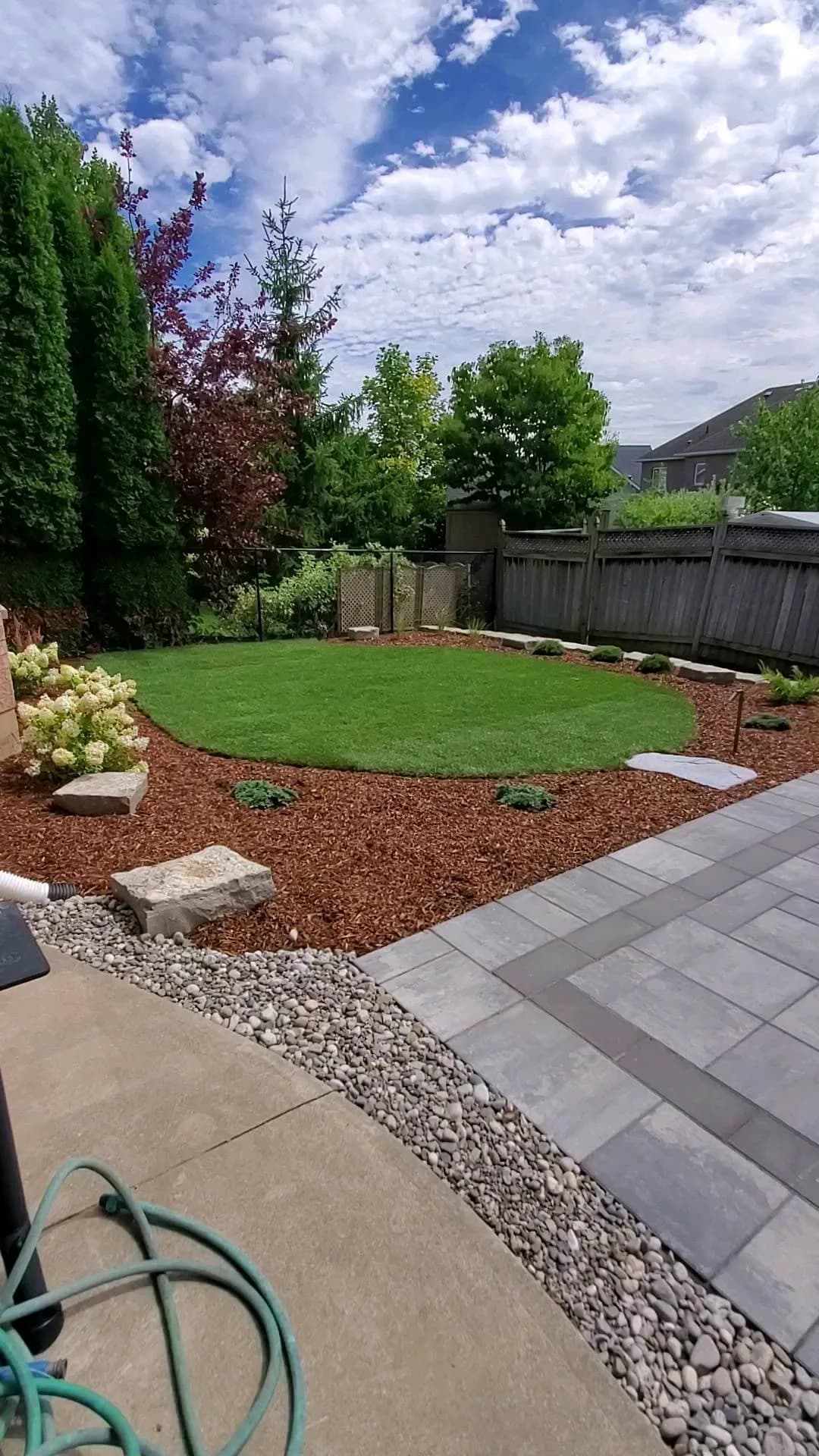 Residential landscaping in Hamilton with circular lawn, mulch beds, and paver patio